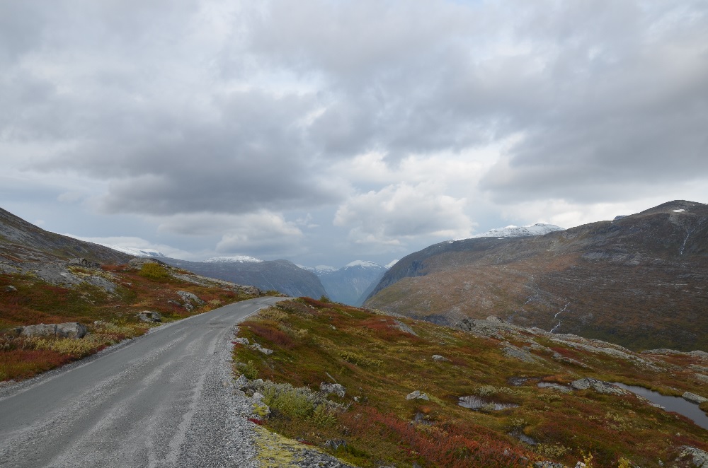 En svingete vei gjennom et fjellandskap med skyer og høstfarger.

