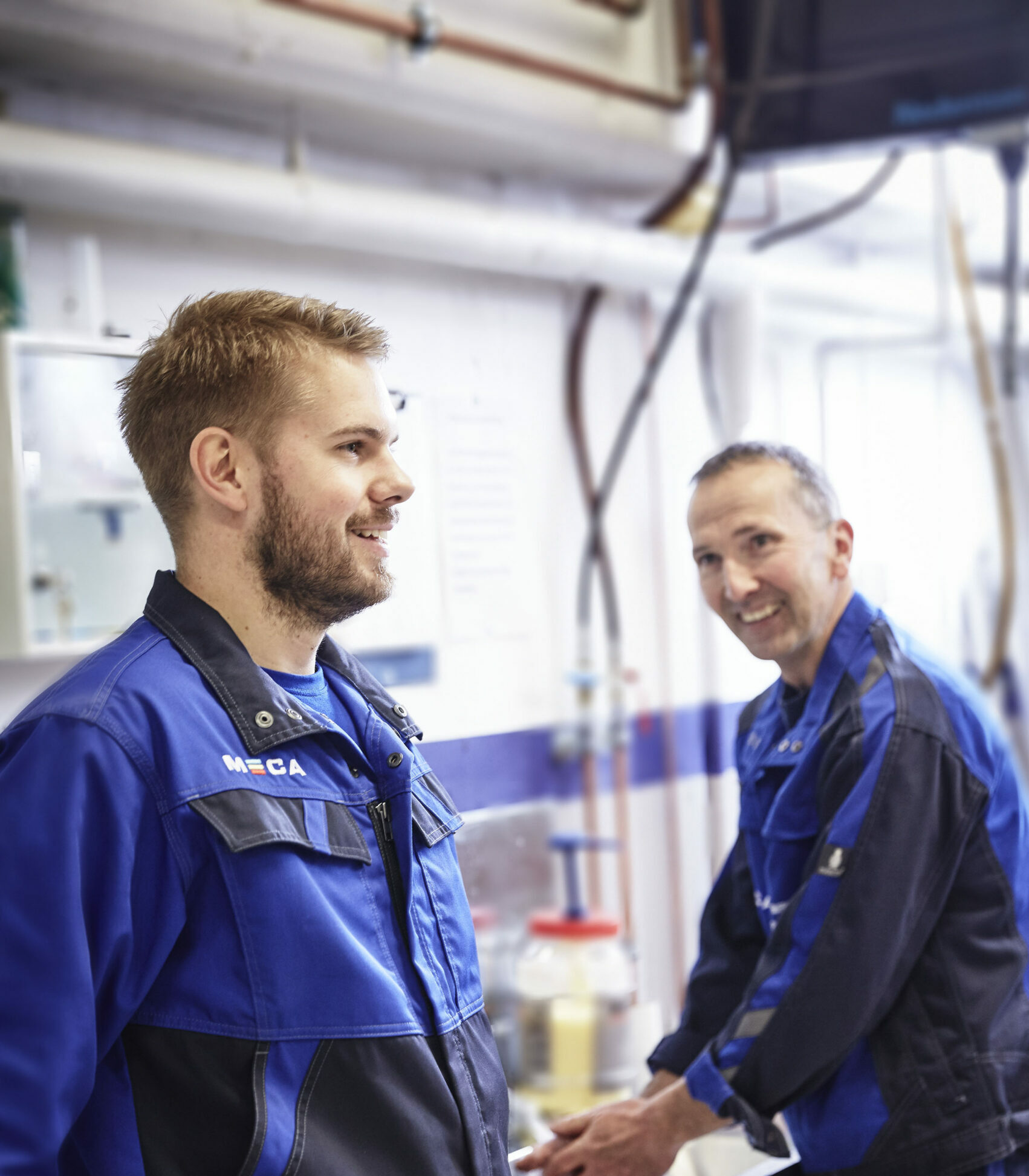 bilmekanikere i bilverksted smiler og snakker