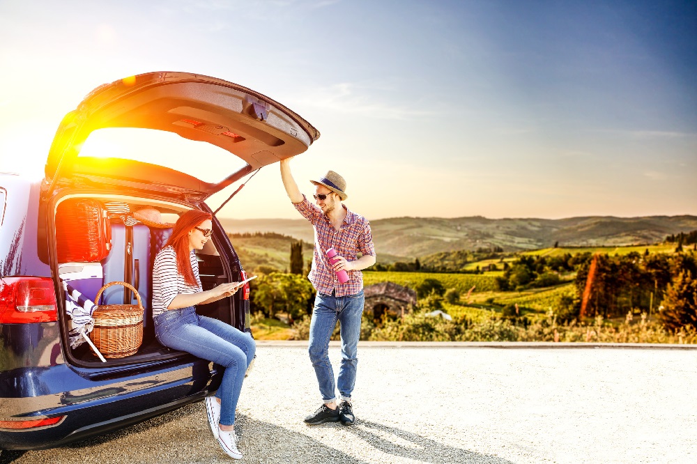 Ferie, to unge mennesker i solnedgang med fullpakket bil