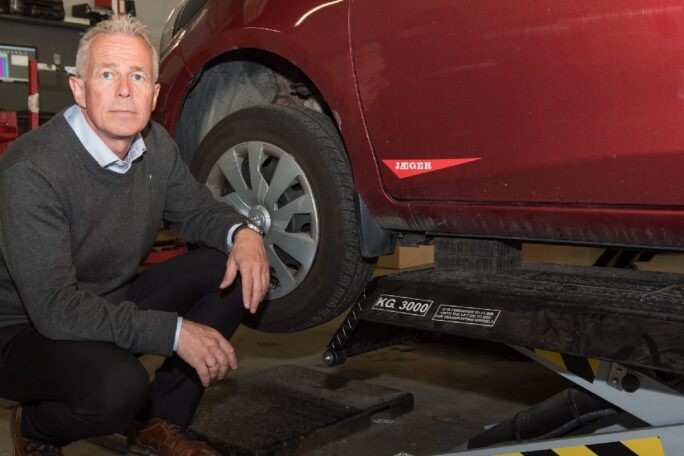 Mann sitter ved framhjulet på en bil