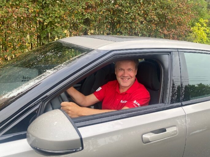 Mann i rød t-skjorte kjører en lys bil