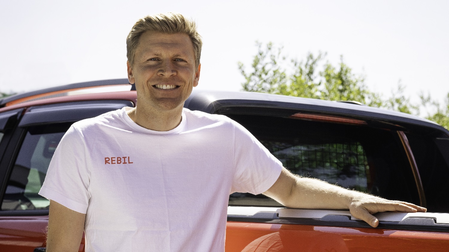 Mann med hvit t-skjorte foran rød bil