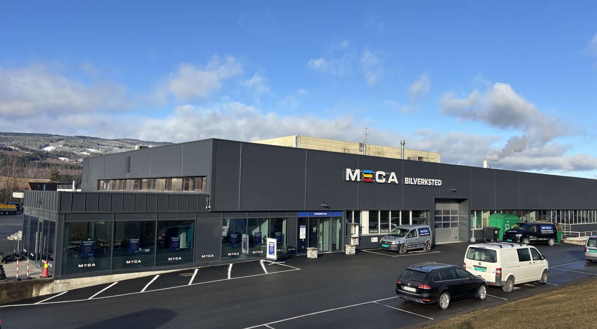 Grått moderne verkstedbygg med MECA Bilverksted skilt på veggen