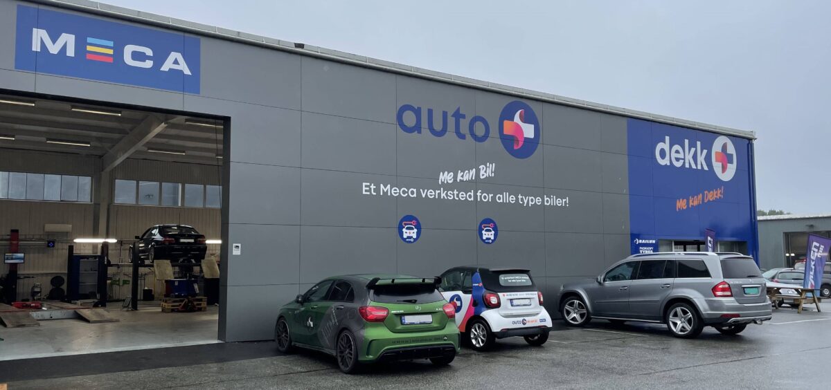 Bilverksted med flere biler parkert utenfor, inkludert en hevet bil inne i verkstedet.