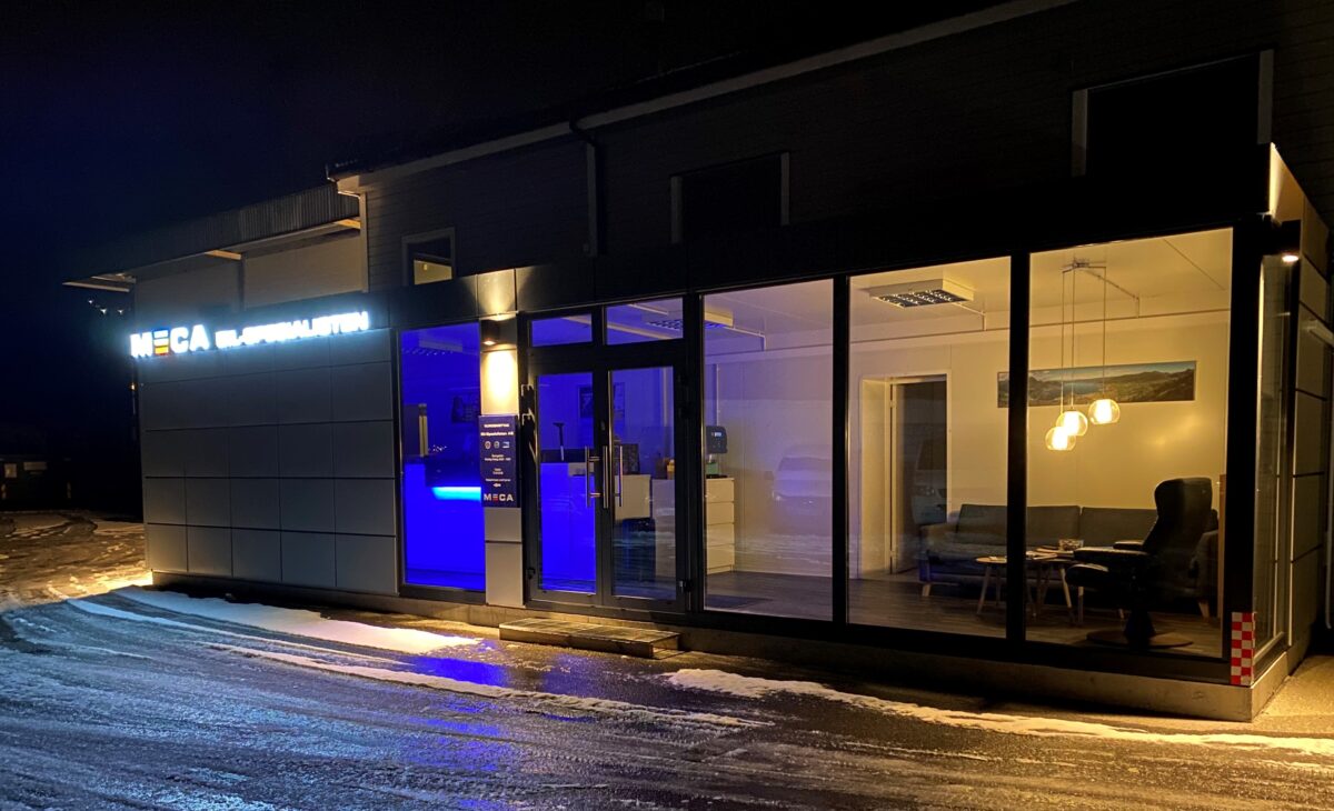 Bilverksted med opplyst inngang og moderne interiør, sett om kvelden.