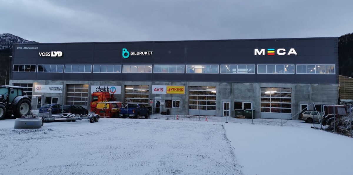 Bilverksted med flere logoer på fasaden, omgitt av snødekt landskap og kjøretøy.