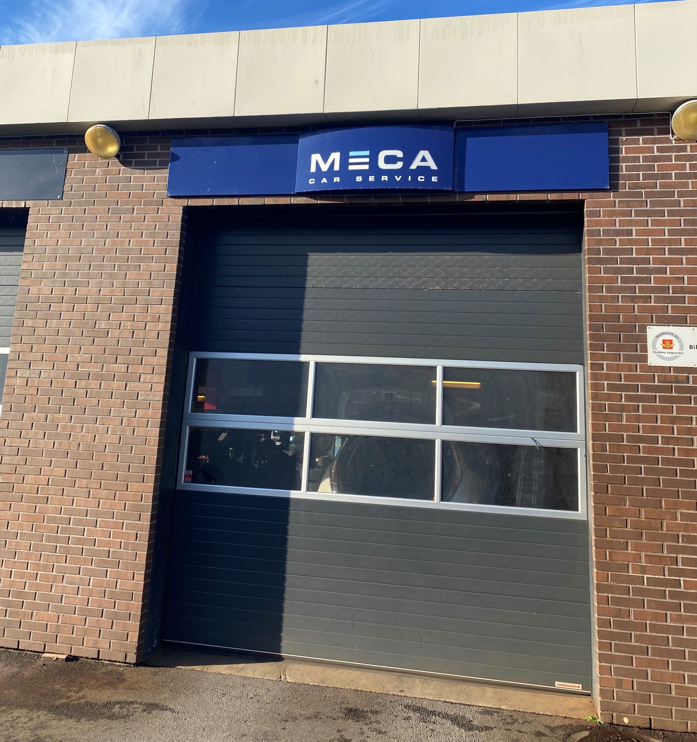 Bygning med MECA Car Service-skilt og lukket garasjeport under blå himmel.