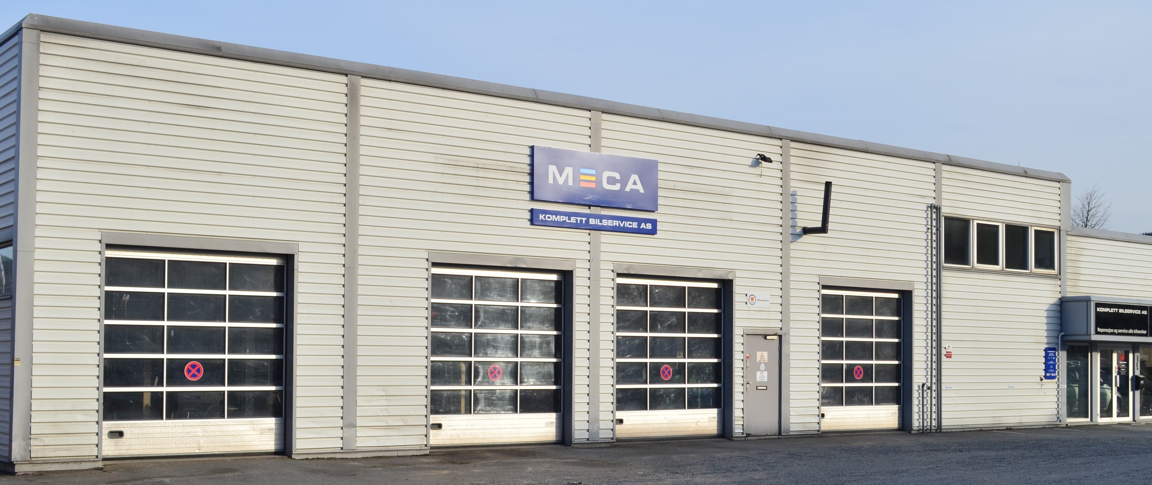 Bilverksted med fire garasjeporter og MECA-skilt på fasaden.
