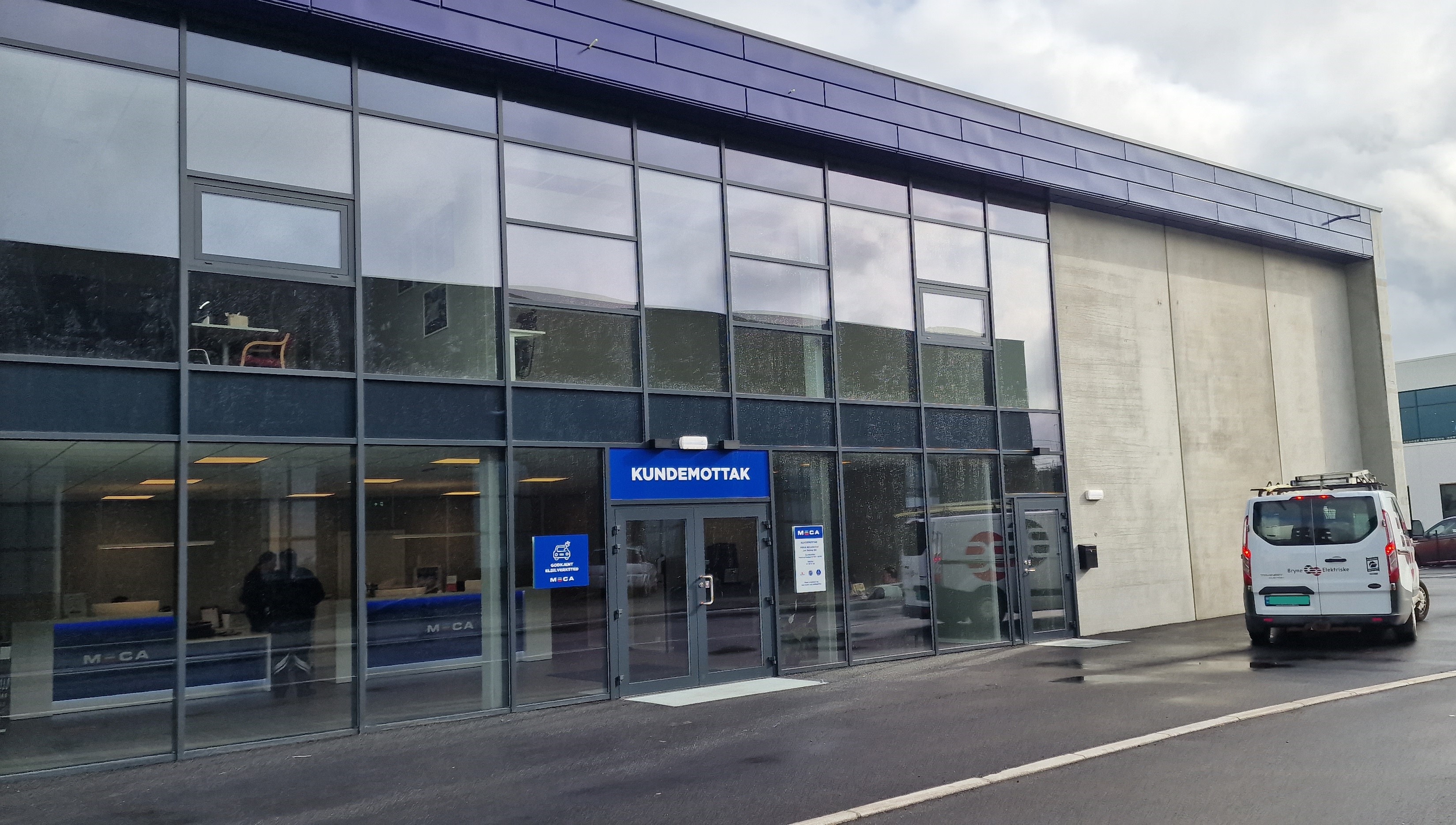 Bilverksted med moderne glassfasade og kundemottak ved inngangen, parkert bil utenfor.