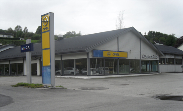 Opel forhandler og MECA Bilverksted, grå bygning foran en grå himmel i bakgrunnen.