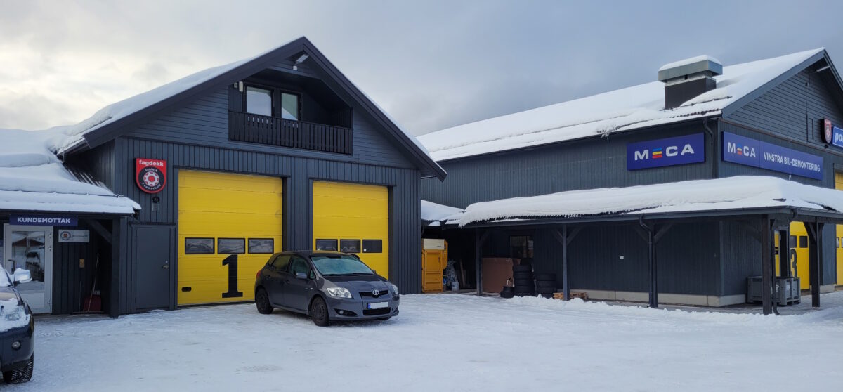 Bilverksted i vinterlandskap med snødekte tak og parkerte biler foran.