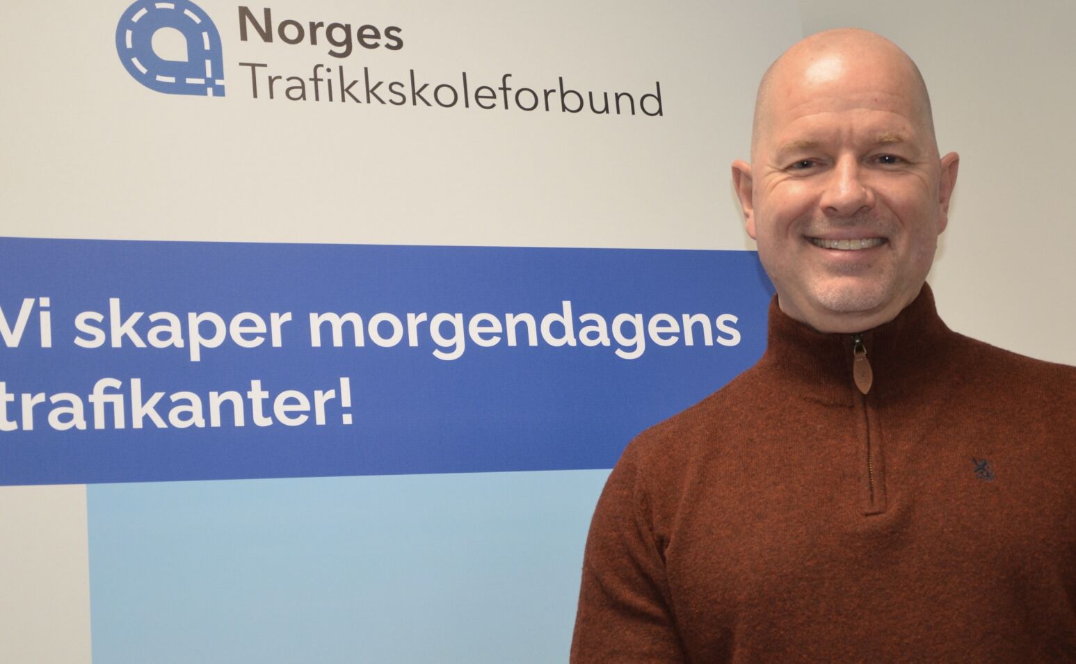 Mann foran skilt med Norges Trafikkskoleforbund
