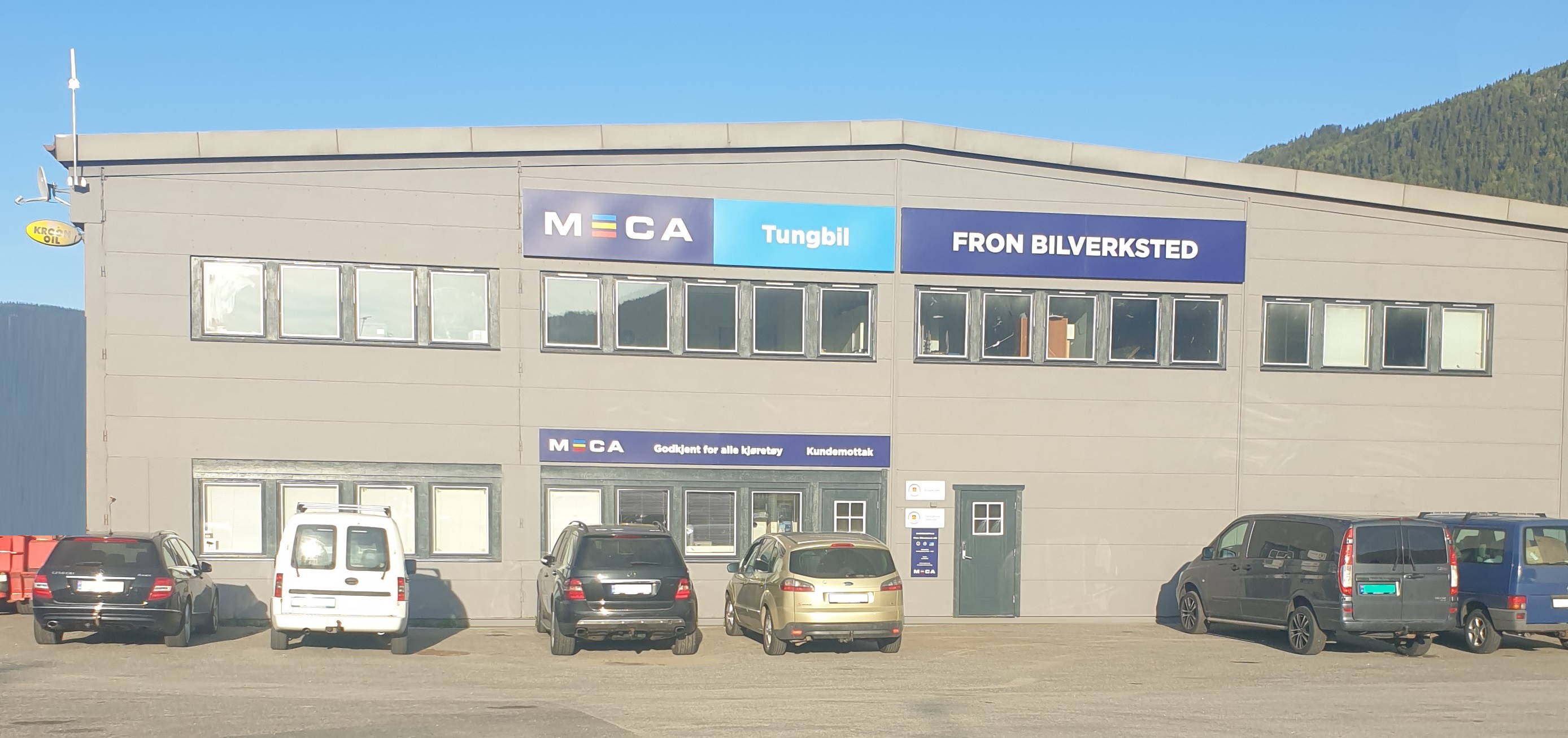 MECA Tungbil verkstedet Fron bilverksted med flere parkerte biler foran en grå bygning i solskinn.