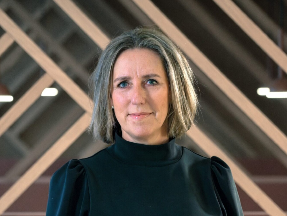 Dame med sort høyhalset bluse foran en moderne trevegg