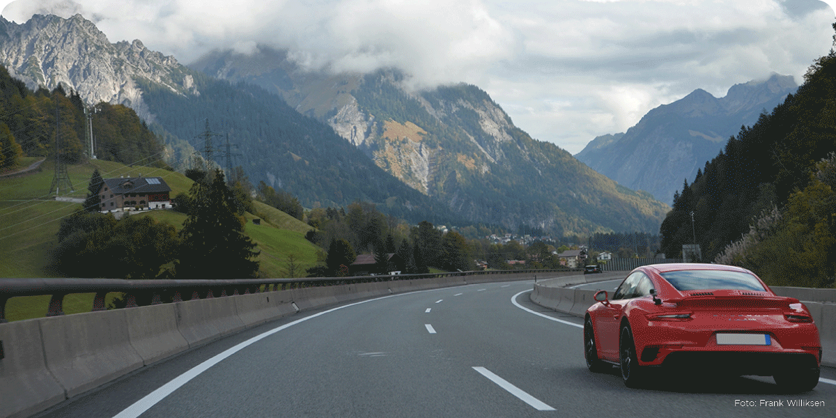 Rød Porsche kjører på fine motorveier med nydelig utsikt over fjellene i Østerrike