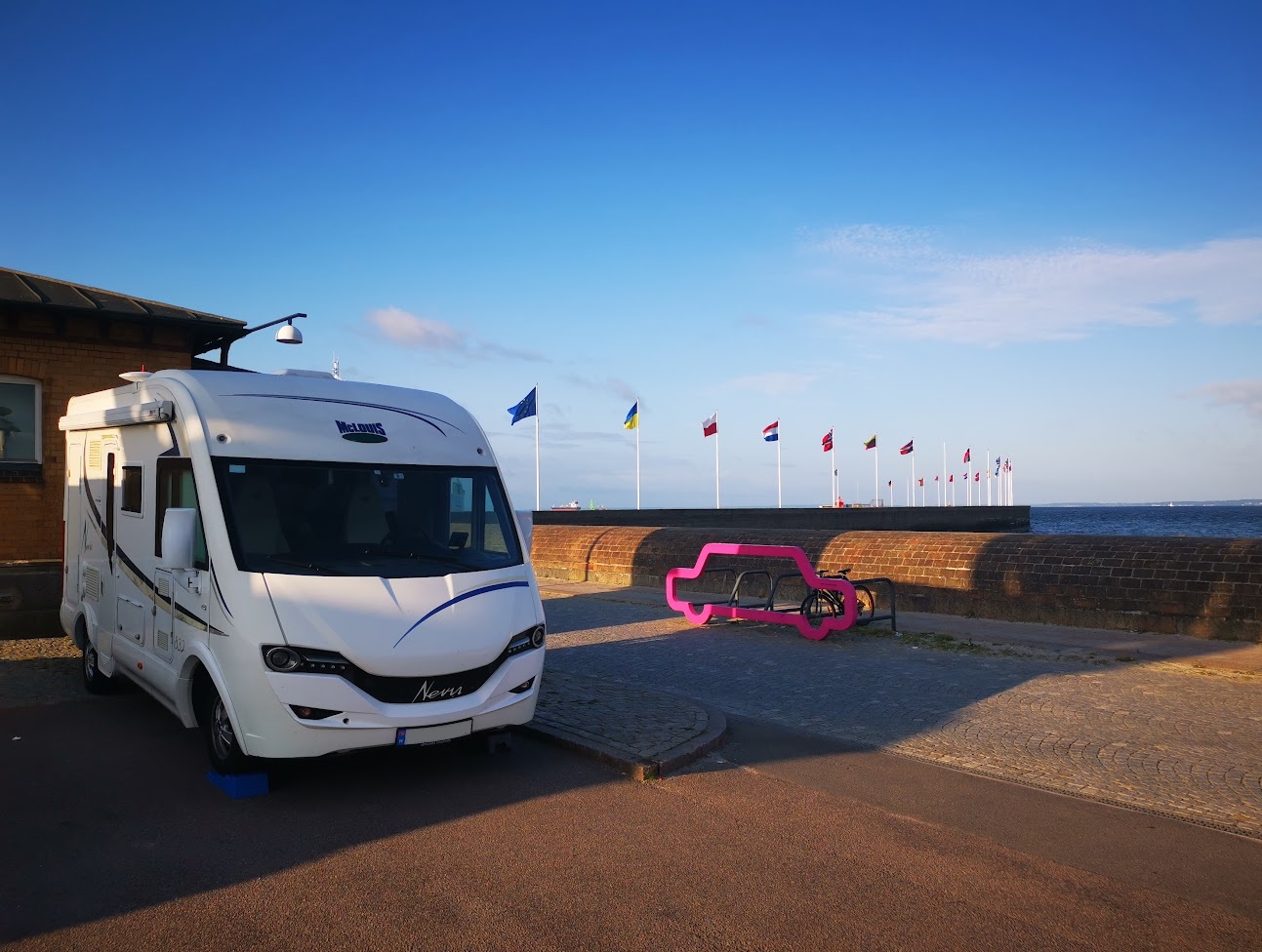 Bobil parkert på havnen med blå himmel og flagg i bakgrunnen