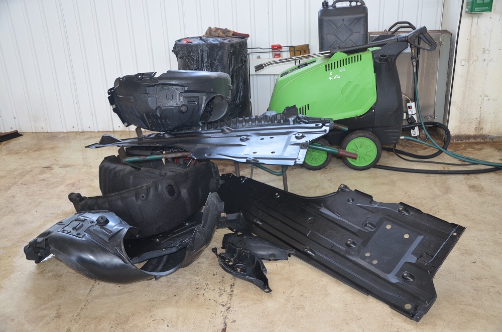 Deksler fra under bilen ligger på verkstedgulvet. Demontert for å gjennomføre antirustbehandling