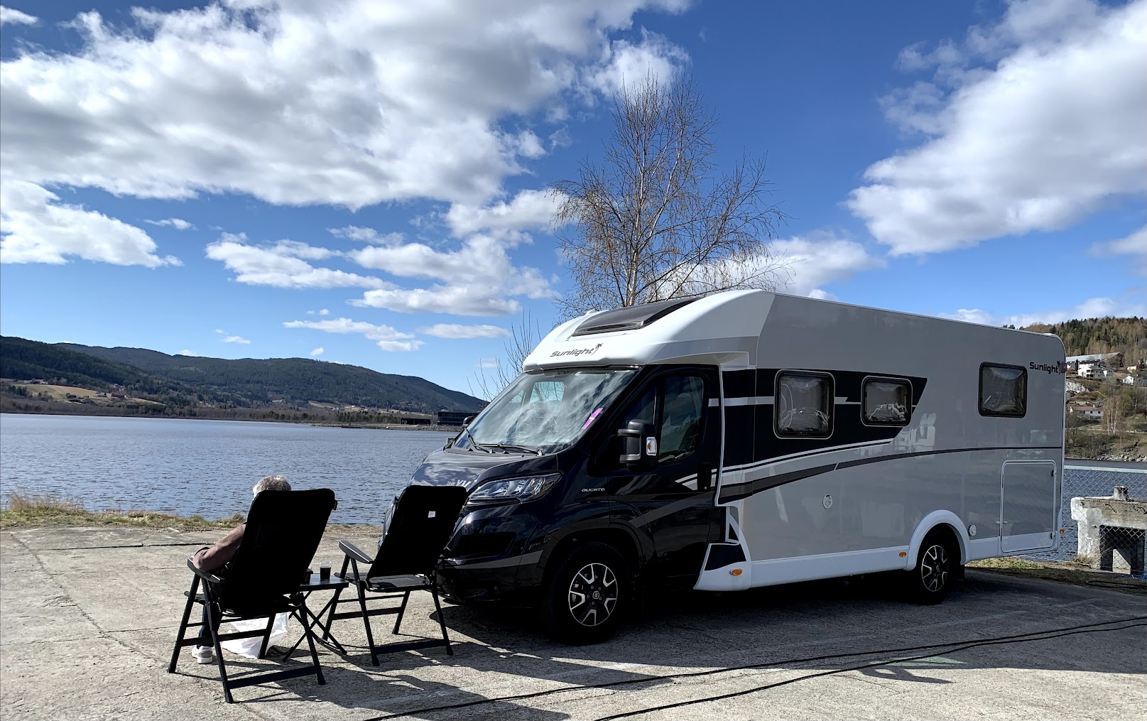 Bobil parkert ved vannet en vårdag med lettskyet vær