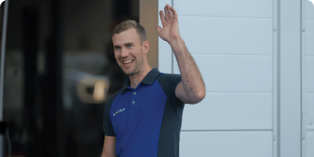 Mekaniker i MECAblå t-shirt, utenfor verkstedet sammen med den kloke MECA uglen