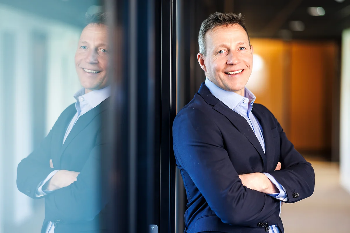 Moderne profilbilde av en blid veksen mann i mørk dress. Gjennskinn i ruten bak han.