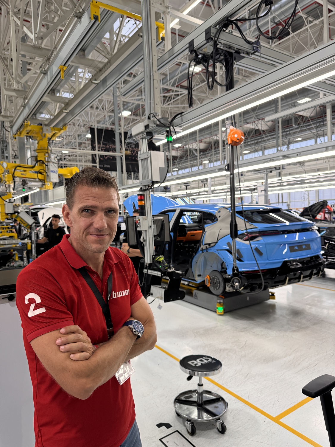 Mann med rød t-skjprte foran en blå bil som holder på og bli mortert, på en bilfabrikk