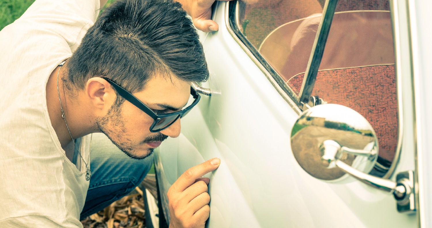 Ung mann med solbriller, sjekker etter flekker på siden av en hvit bil