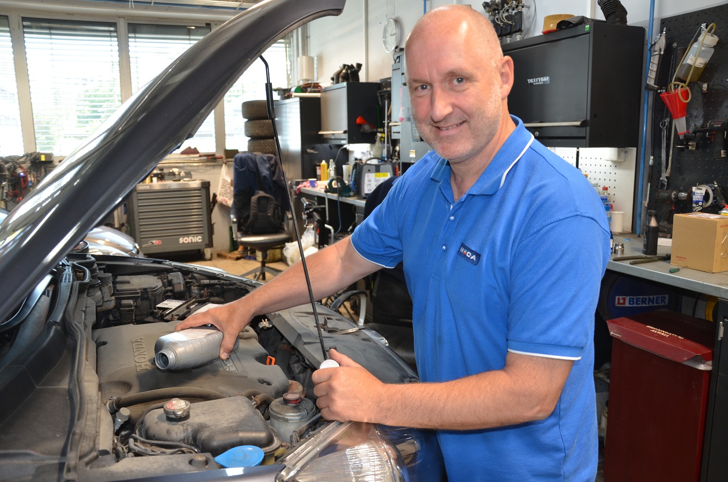 Mekaniker i blå t-shirt med MECA logo foran motorrommet på en bil