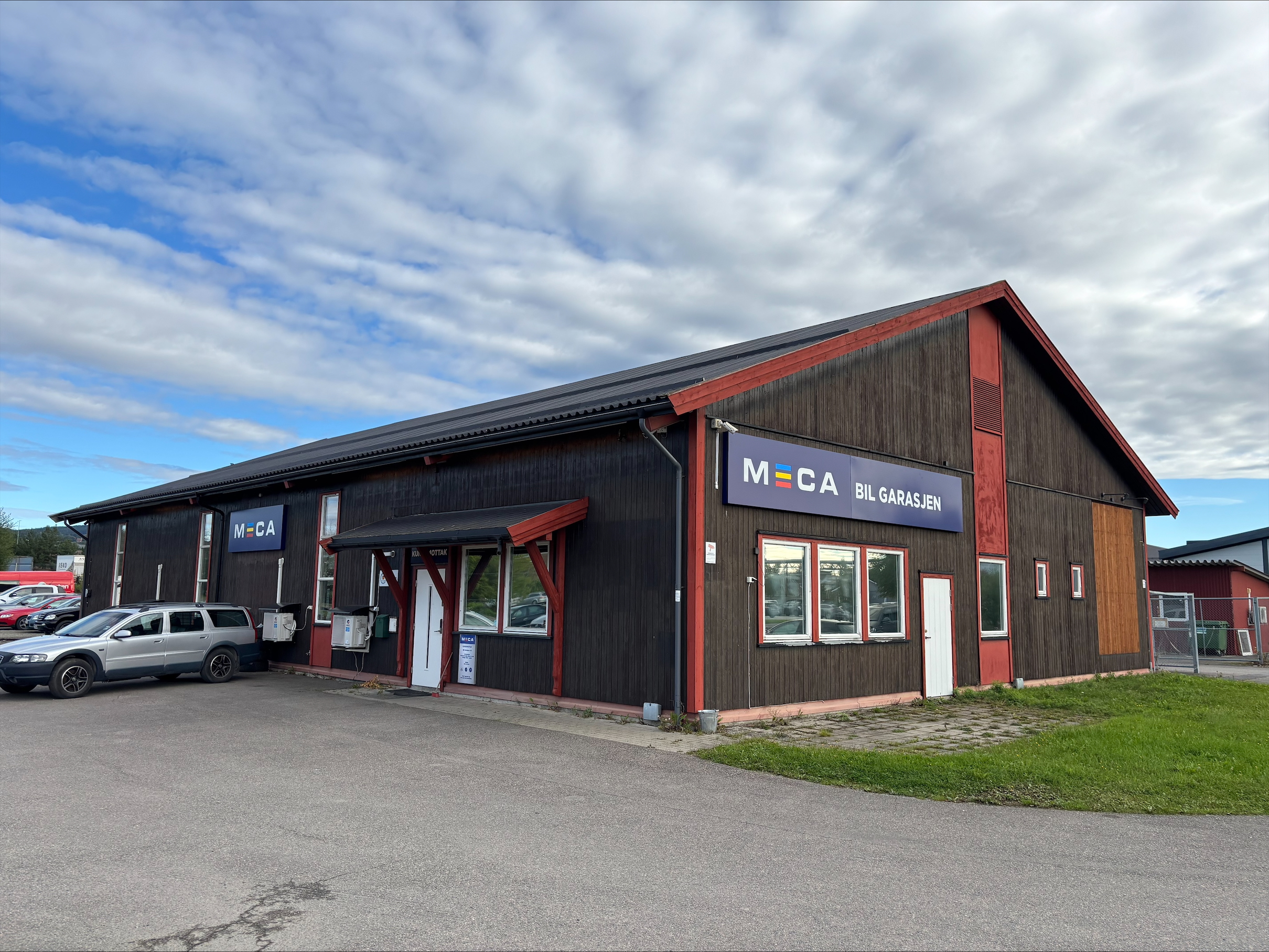 Brun stor verkstedbygning i treverk, med MECA og Bil garasjon logo på veggen