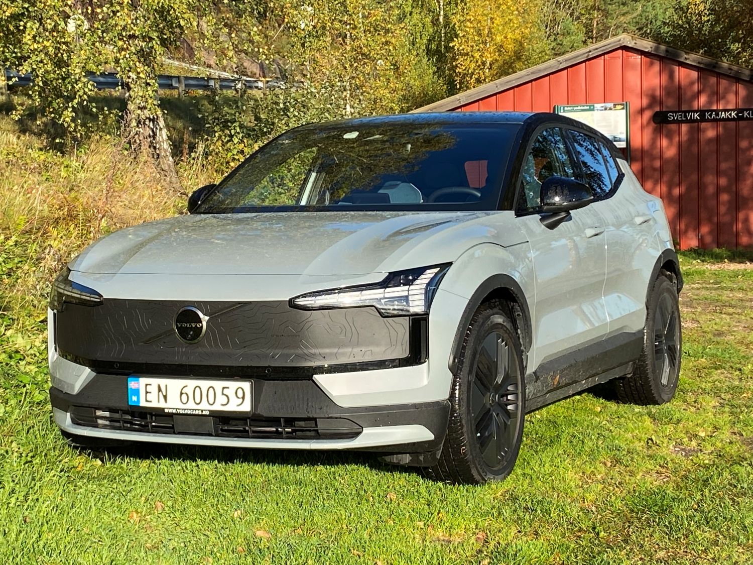 En grå Cross Country-modell av Volvo EX30, på en grønn plen foran en rød hytte