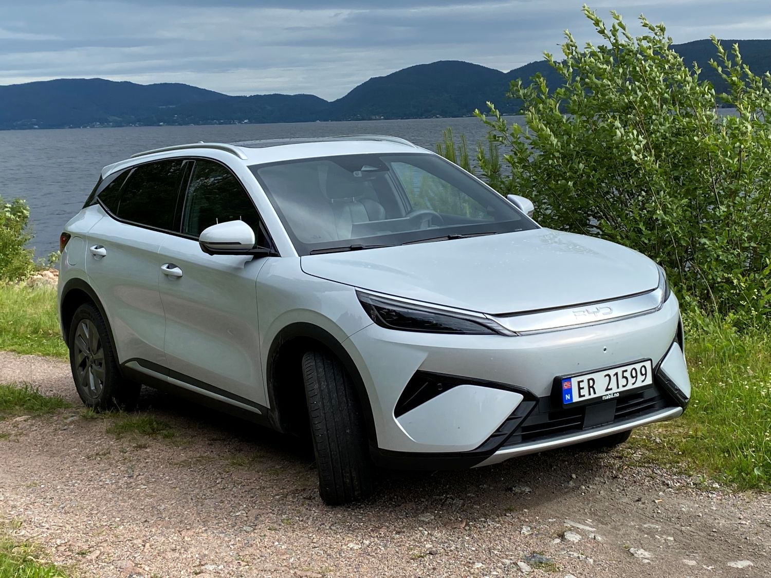 Hvit BYD foran en innsjø med fjell i bakgrunnen